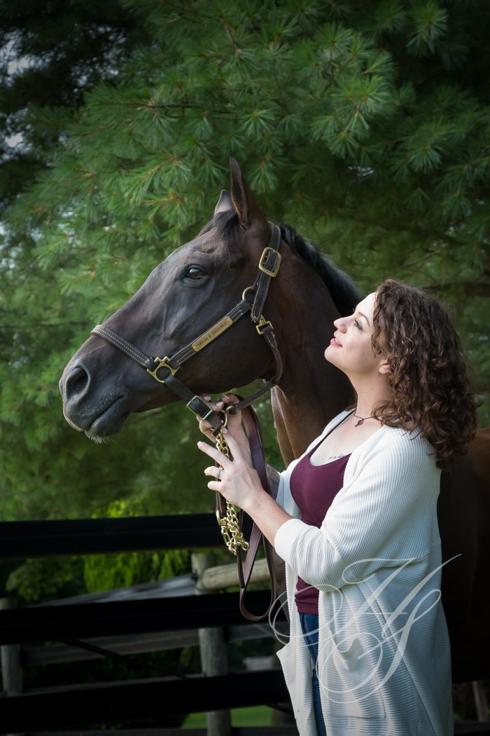 A woman standing next to a horse in the woods.