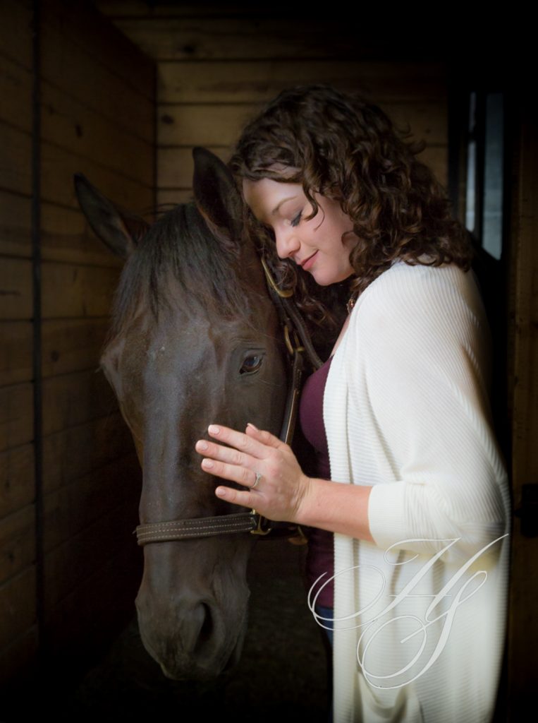 A woman standing next to a horse in a stable.