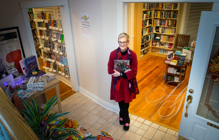 A woman in red jacket holding book near bookshelves.